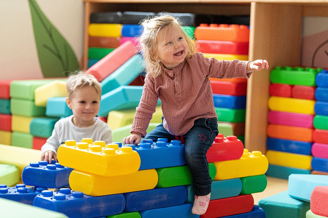 Toddler laughing on colorful building blocks, with another boy beside