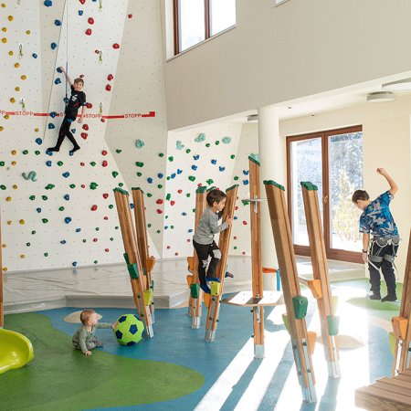 Kids playing and climbing in a bright indoor hall with bouldering wall
