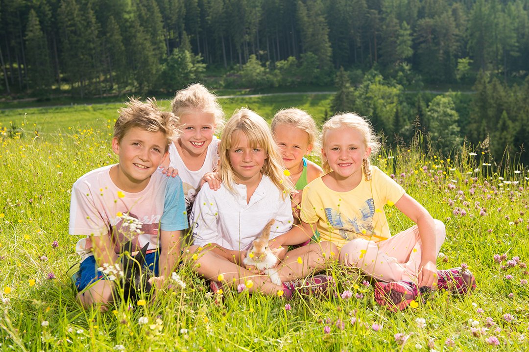 Children sit together in a flower meadow, cuddling a rabbit in the sunshine.