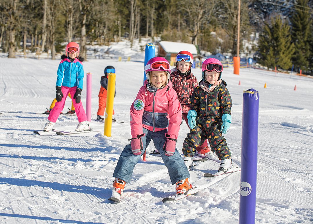 Children skiing through colorful posts on a sunny practice slope.