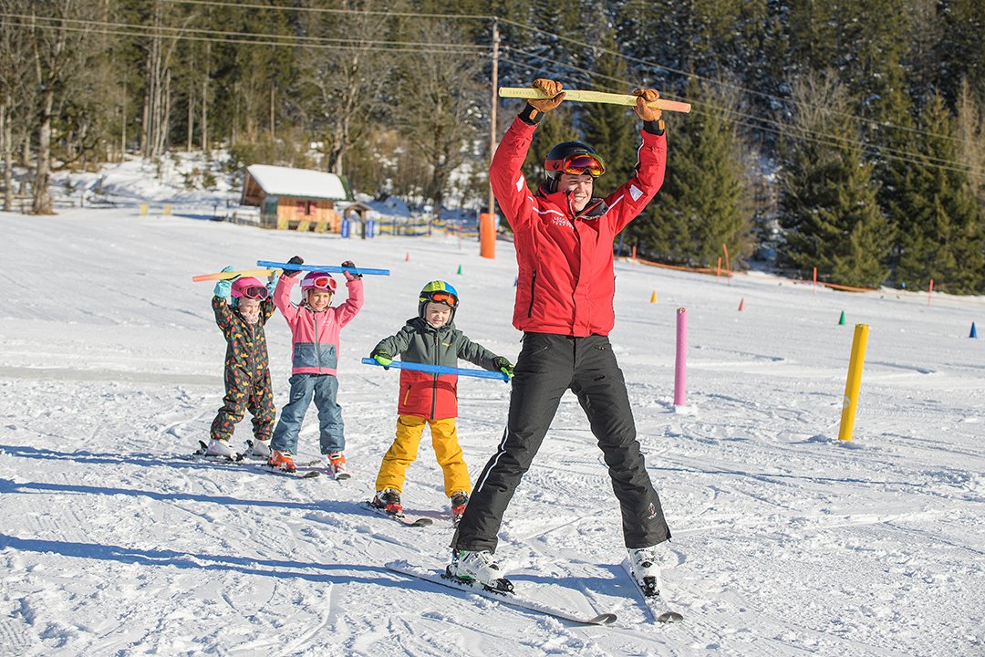 Ski instructor and kids raising sticks while skiing in line.
