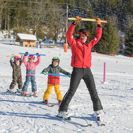 Ski instructor and kids raising sticks while skiing in line.