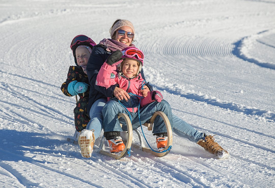 Smiling woman sledding with two happy children on snow.